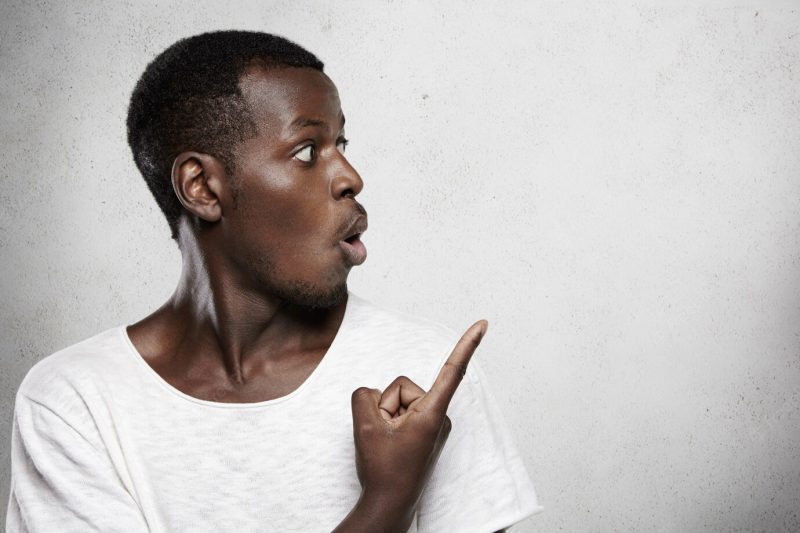 Headshot of good-looking young dark-skinned customer looking away at blank wall, pointing his finger at copy space for your promotional content, saying wow or omg, surprised with information Free Photo