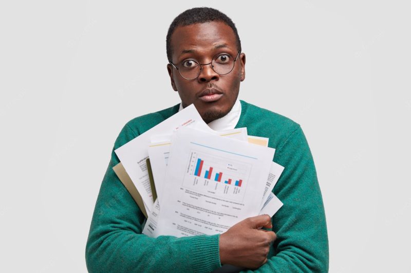 Headshot of surprised businessman carries paper documents with graphics, busy working, makes project has dark healthy skin, isolated over white space Free Photo