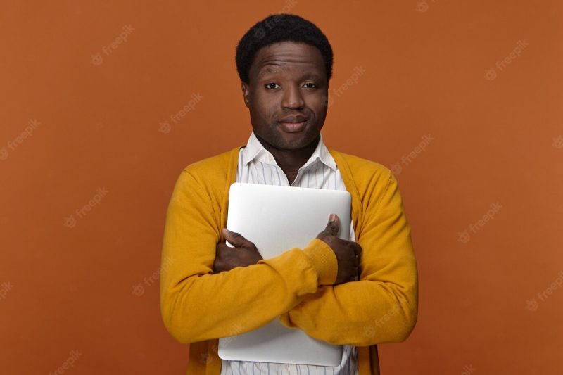 Horizontal image of successful confident handsome young afro american businessman embracing portable computer having pleased satisfied facial expressions, smiling, enjoying electronic device Free Photo