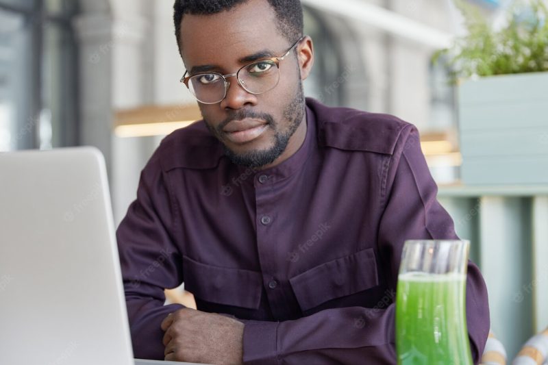 Horizontal shot of attractive dark skinned male manager does work on portable laptop computer, has thoughtful focused serious Free Photo