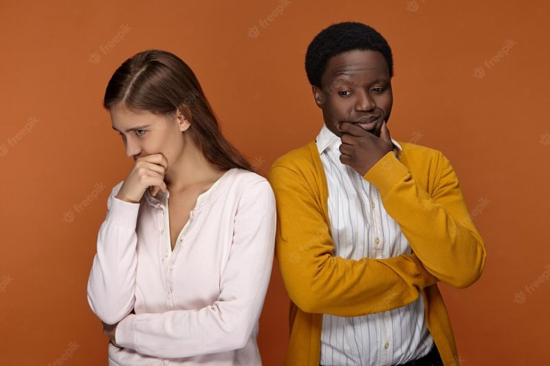 Horizontal shot of attractive young european woman and handsome afro american man in neat casual clothes having pensive thoughtful facial expressions, touching faces, being deep in thoughts Free Photo