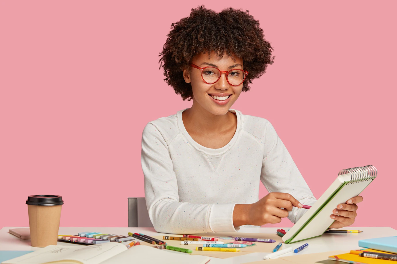 Horizontal Shot Cheerful Afro African Painter Wears Red Rim Spectacles Makes Sketches Spiral Notebook With Pencil Enjoys Aromatic Beverage Surrounded With Stationary Smiles Positively 273609 29135