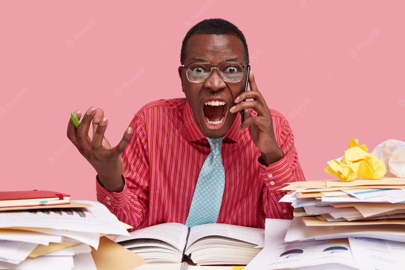 Horizontal shot of mad displeased dark skinned man worker opens mouth widely, has outraged facial expression, speaks via smart phone, has failure Free Photo