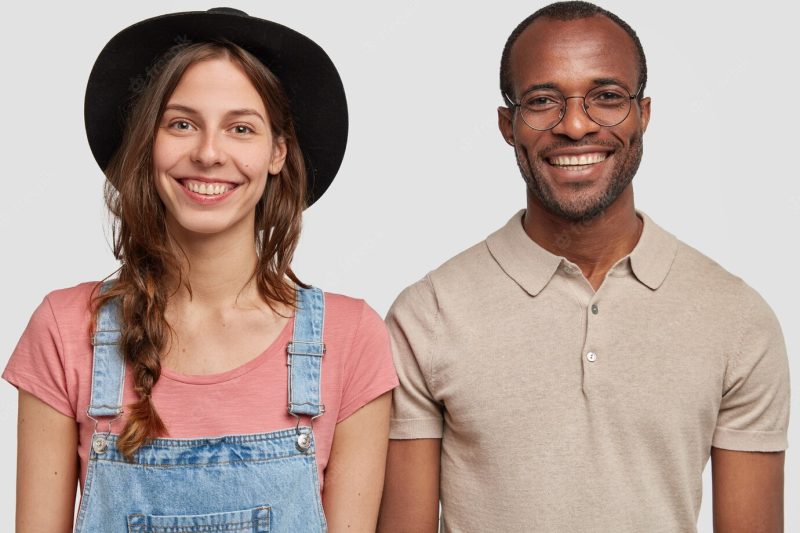 Horizontal shot of multi-ethnic woman and man stand together against white wall, smile broadly, isolated Free Photo