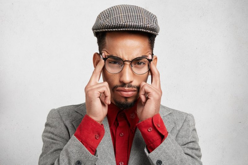 Horizontal shot of pensive mixed race man dressed formally, keeps fingers on temples, Free Photo