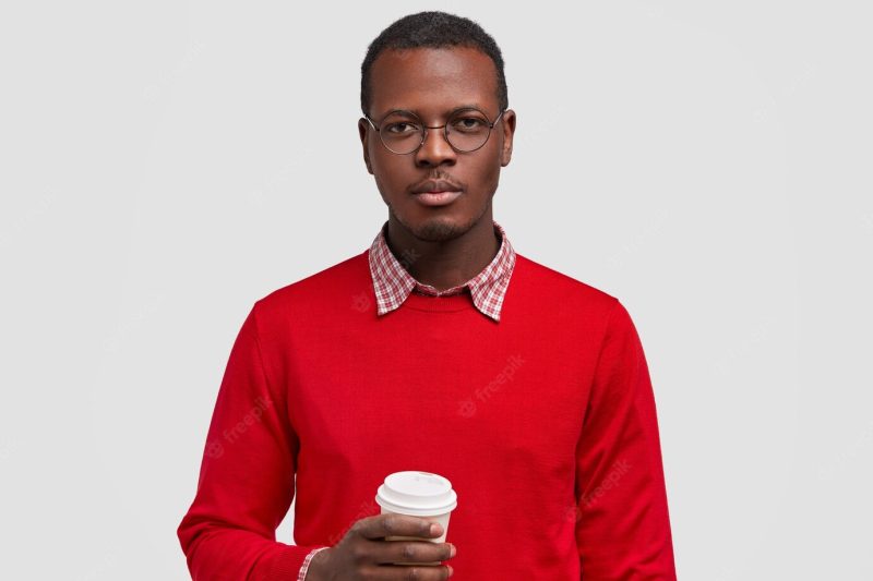 Horizontal shot of serious dark skinned man holds disposable cup of coffee, dressed in red jumper, looks confidently Free Photo