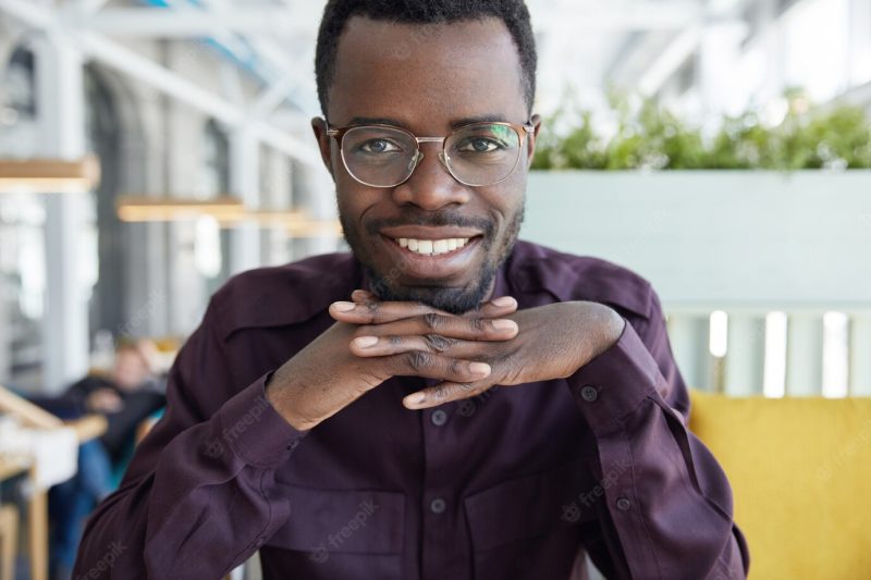 Horizontal shot of successful dark skinned entrepreneur in glasses and purple shirt, looks happily at camera, shows even white teeth Free Photo