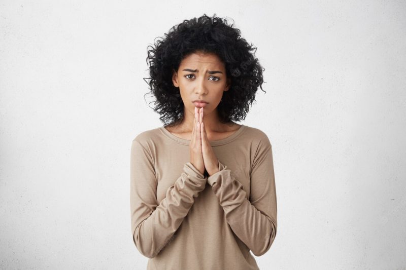 Human emotions, feelings, reaction and attitude. beautiful student woman with afro hairstyle holding hands in prayer, begging professor to give her another chance on examination, having beseeching look Free Photo