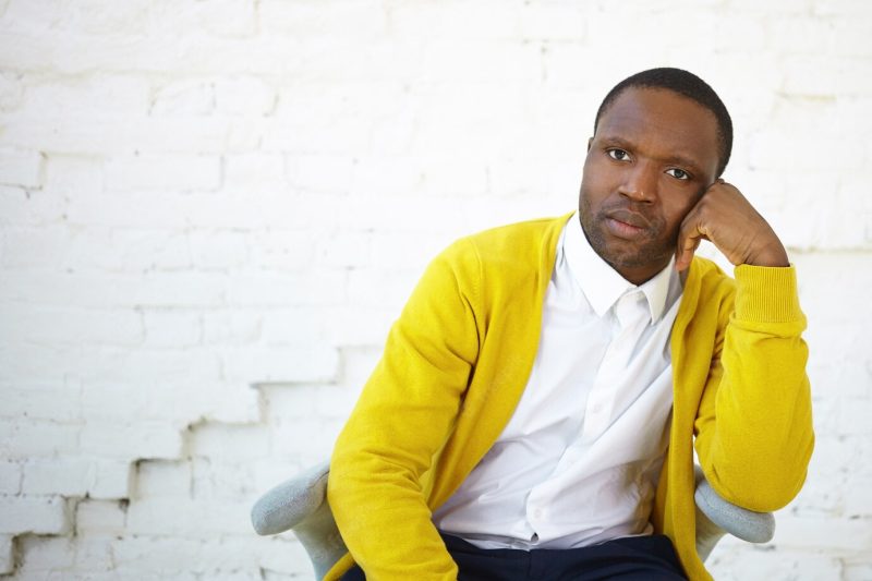 Human facial expressions, emotions and feelings. handsome african man having sad disappointed look, keeping hand on his face, sitting in chair at white brick wall with copy space for your text Free Photo