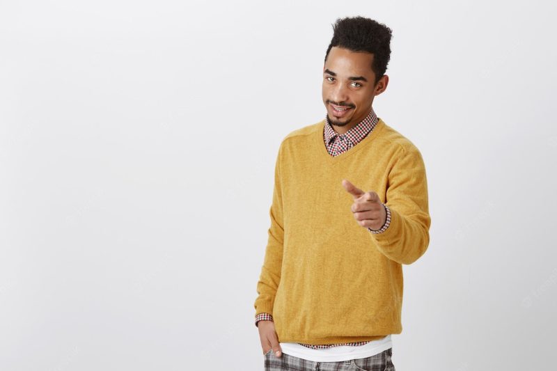 I choose you to work with me. Portrait of attractive American male model with afro haircut in yellow sweater pointing with confident and charming expression, flirting Free Photo