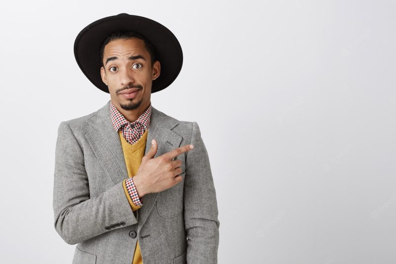 Indecisive African American businessman in suit pointing upper right corner, looking doubtful Free Photo