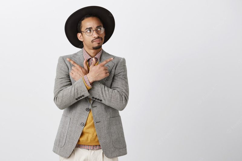 Indecisive African American man making decision, looking upper right corner thoughtful while choosing, pointing sideways Free Photo