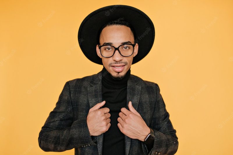 Indoor photo of fascinating african young man wears stylish wristwatch.black guy in glasses posing with gently smile. Free Photo