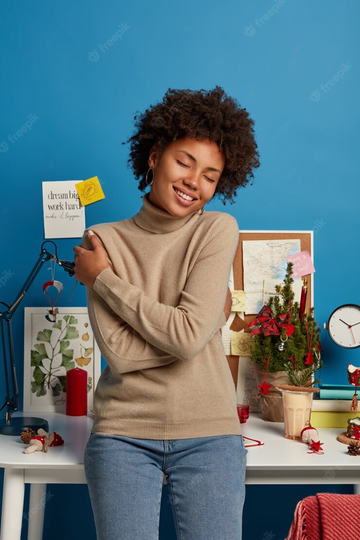 Indoor Shot Pleased Glad Woman Embraces Herself Feels Comfort New Soft Jumper Smiles Toothily Closes Eyes With Pleasure Stands Near Desktop Against Blue Wall Recalls Nice Moment 273609 37655