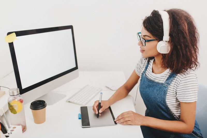 Inspired young woman in striped shirt looking at computer screen and working with tablet Free Photo