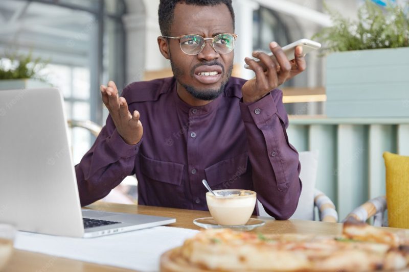 Irritated dark skinned young male enterpreneur being on working place feels very stressed and angry as can`t manage to do all work Free Photo