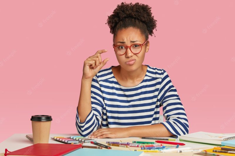 Isolated shot of displeased dark skinned woman shows something tiny with hand Free Photo