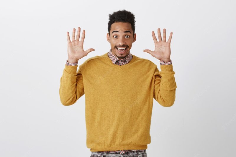 Jazz hands always in trend. portrait of happy emotive young male with afro haircut raising palms and smiling broadly, surrendering or expressing friendliness and good mood Free Photo