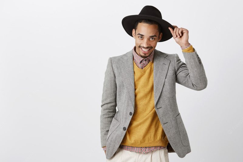 Ladies, how are you. portrait of flirty handsome african-american male holding hat and saluting with passionate gaze, smiling broadly, being confident while greeting beautiful woman Free Photo