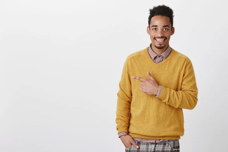 Look at this hot girl. portrait of happy good-looking african man with afro haircut in stylish yellow sweater pointing left and smiling positively, being satisfied discussing interesting concept Free Photo