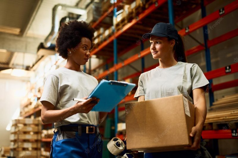 Low angle view of female workers communicating while preparing packages for a delivery in distribution warehouse Free Photo