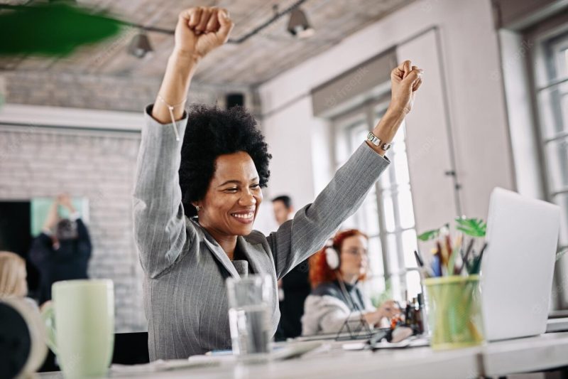 Low angle view of happy black businesswoman working in the office and celebrating her success with raised arms Free Photo