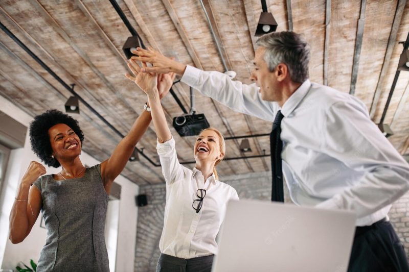 Low angle view of happy colleagues celebrating business success and having fun in the office Free Photo