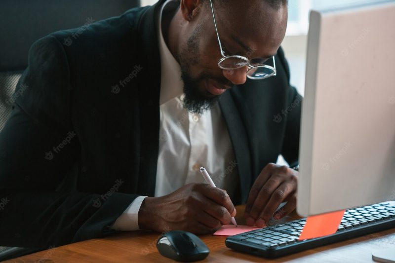 Making notes. African-American entrepreneur, businessman working concentrated in office. looks serious and busy, wearing classic suit, jacket. Free Photo