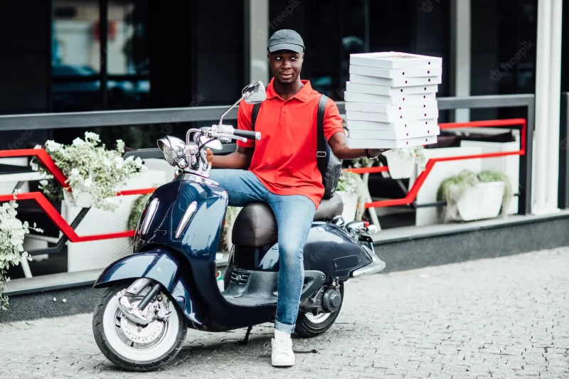 Male courier carries heavy parcel boxes drives slowly on motorbike wears protective helmet on head Free Photo