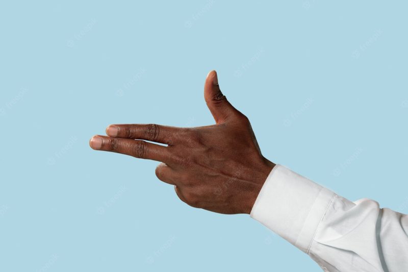 Male hand in white shirt demonstrating a gesture of gun, handgun or pistol isolated on blue background. Free Photo