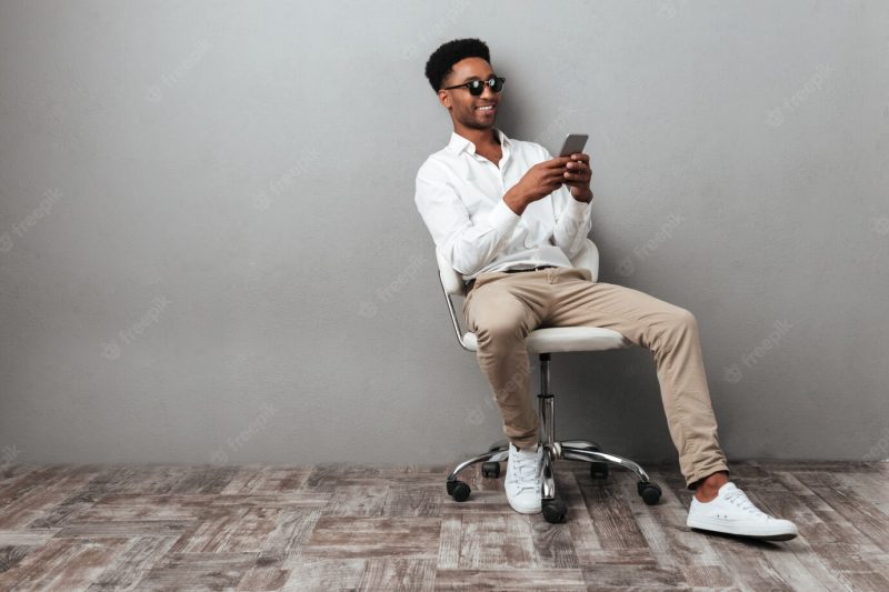 Man sitting in a chair and holding mobile phone Free Photo