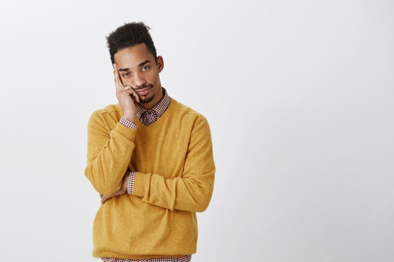 Man wants to be somewhere else. bothered attractive young man with afro hairstyle leaning head on palm, feeling bored and indifferent, expressing desire to leave and annoyance over gray wall Free Photo