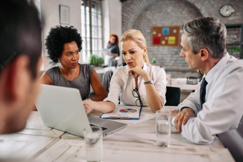 Mid adult businesswoman talking to her colleagues and while using laptop and pointing on the screen in the office Free Photo