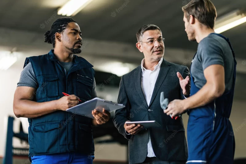 Mid adult manager using digital tablet while talking to car mechanics in auto repair shop Free Photo