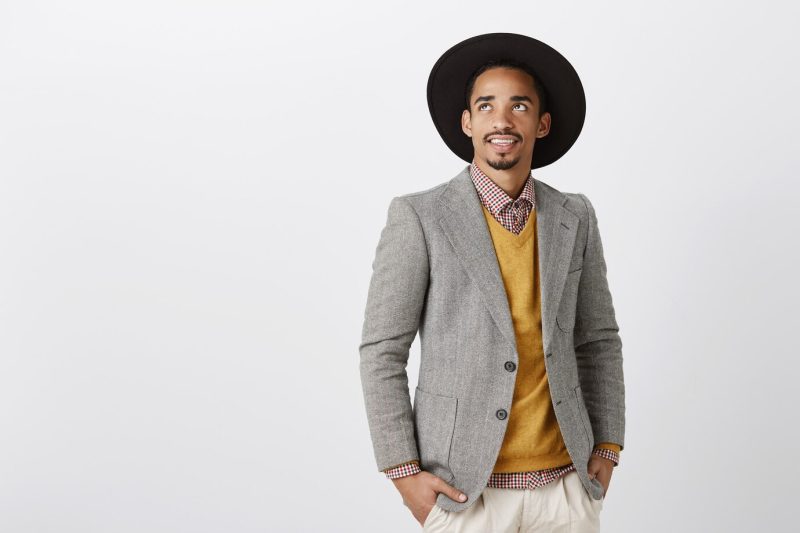 Nice day to earn billions. portrait of wealthy handsome businessman in stylish formal outfit and hat looking up, being interested and entertained with curious thing, dreaming over gray wall Free Photo