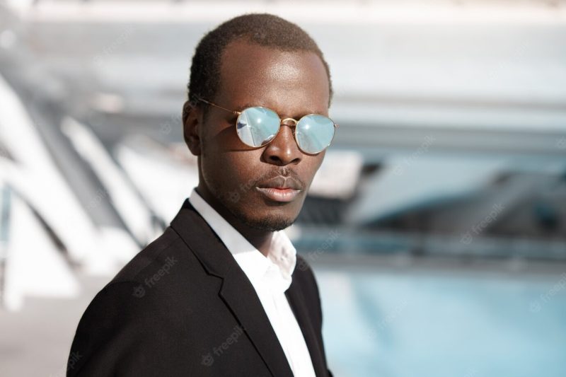 Close up highly-detailed shot of handsome serious Afro american office worker in formal wear and mirrored lens shades posing in urban surroundings, thinking about prospects and possibilities at work Free Photo