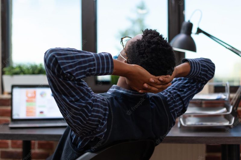 Overworked employee wearing covid protection mask taking a nap at work in office chair. tired startup business owner stretching and taking a break from working on laptop with charts. Free Photo