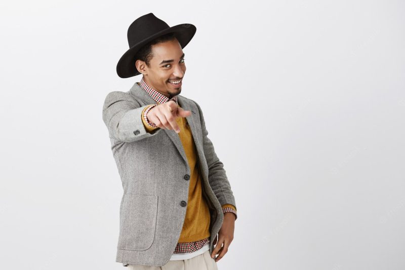 Passionate confident dark-skinned male choosing you. portrait of charming African-American in fashionable hat and jacket, pulling hand and pointing with sensual flirty smile over gray wall Free Photo