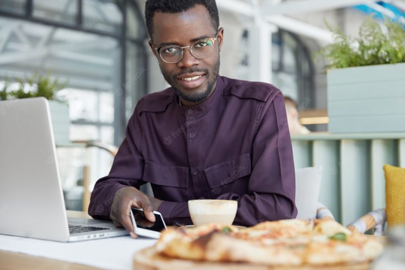 People, business and technology concept. dark skinned delighted young male in formal clothing, holds modern smart phone as waits for call Free Photo