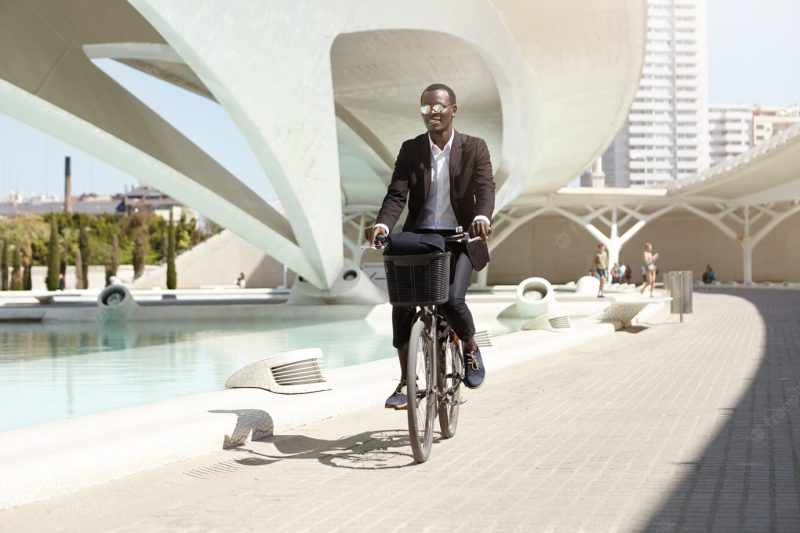 People, lifestyle, transport and ecology. handsome cheerful smiling young dark-skinned office worker dressed formally commuting to work on his retro black bicycle, enjoying sunny summer morning Free Photo