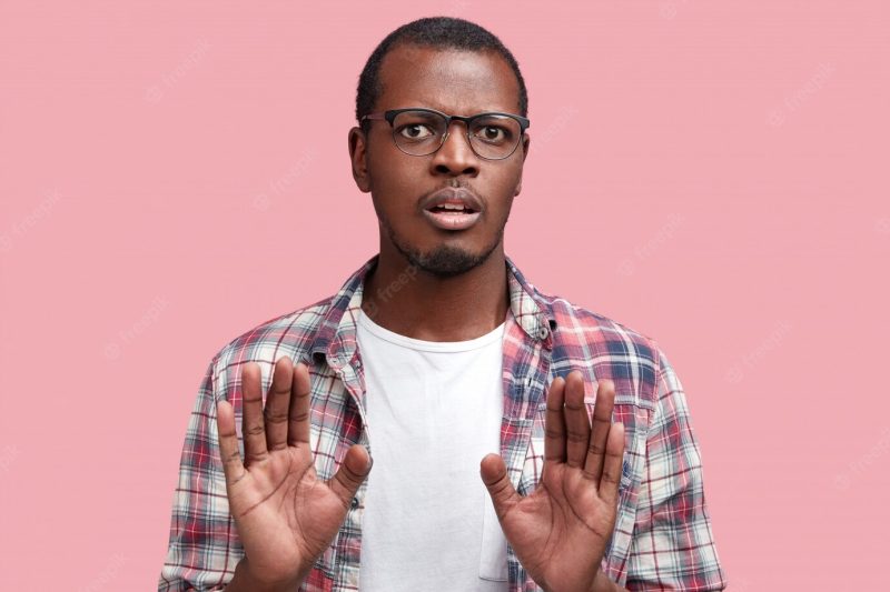 Photo of discontent dark skinned male with displeased expression, makes refusal gesture, asks to stop it. handsome African American man in spectacles gestures Free Photo