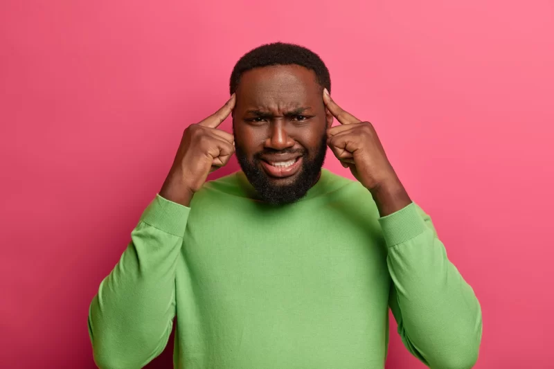 Photo of intense bearded man worker suffers from headache because of long hours of working, keeps index fingers on temples, smirks face Free Photo