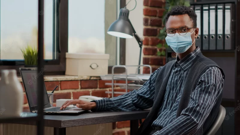 Portrait of accountant working on commercial report project, using laptop and wearing face mask in office. financial consultant analyzing sales growth on computer at startup company. Free Photo