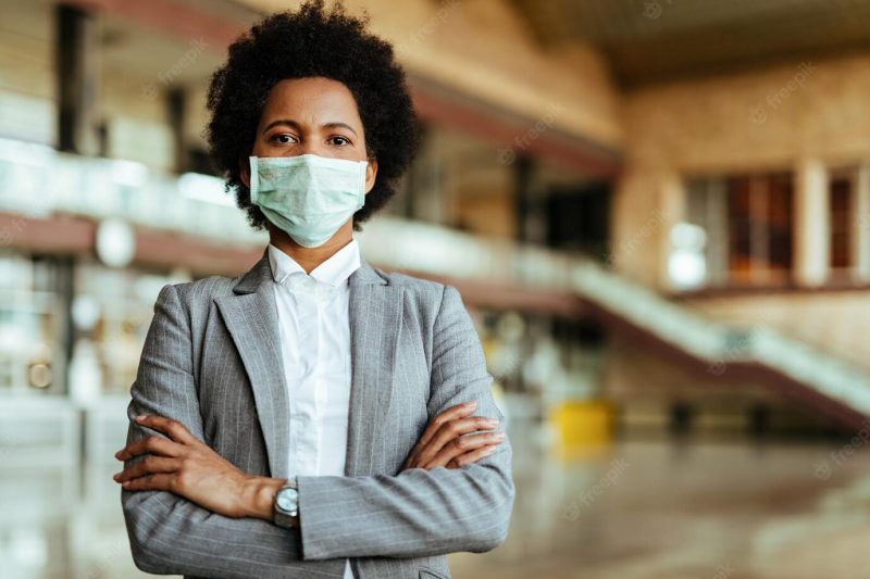 Portrait of african american woman wearing protective mask while standing with arms crossed at the airport during virus epidemic Free Photo