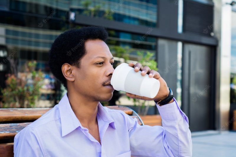 Portrait of afro businessman taking a break from work and drinking a cup of coffee outdoors. business concept. Free Photo