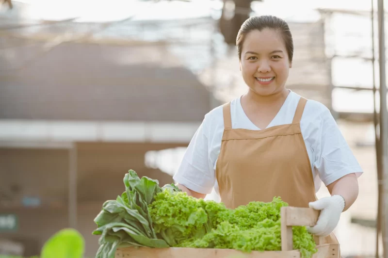 Portrait of asian farmer woman holding wooden box full of fresh raw vegetables. organic farm concept. Free Photo