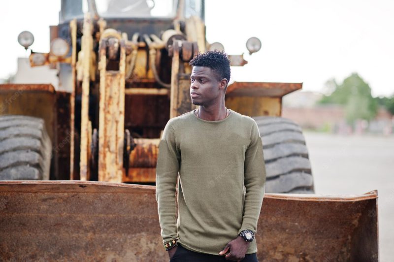 Portrait of an attractive black african american man posing next to the industrial machinery Free Photo