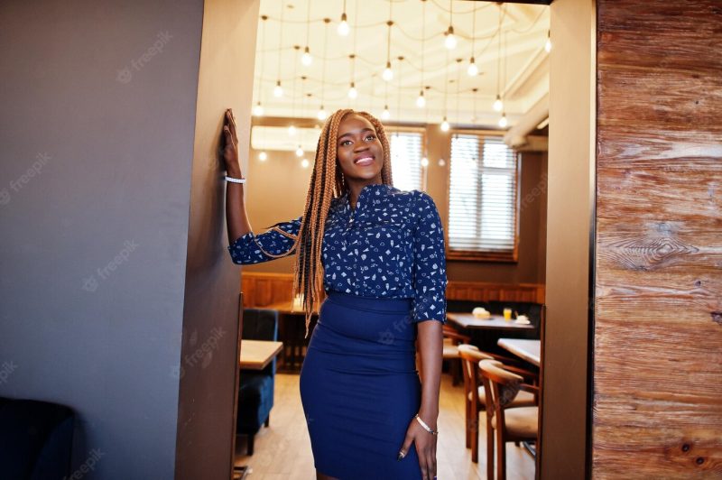 Portrait of beautiful young african business woman wearing blue blouse and skirt posing in cafe Free Photo