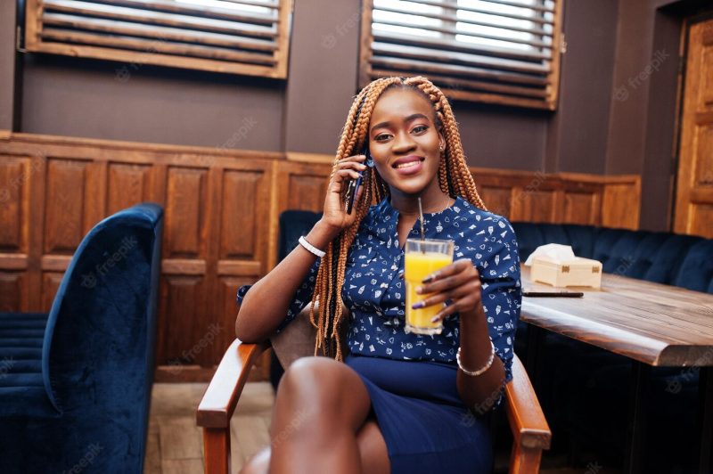 Portrait of beautiful young african business woman wear a blue blouse and skirt sitting with juice in cafe and speak on phone Free Photo