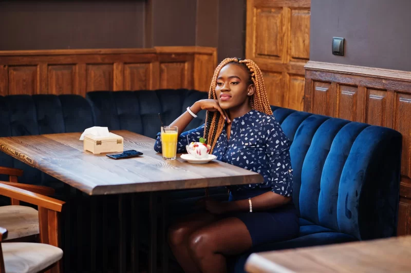 Portrait of beautiful young african business woman with dreadlocks wearing  blue blouse and skirt sitting in cafe with ice cream and pineapple juice Free Photo